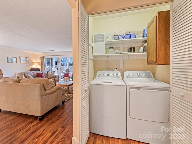 clothes washing area featuring cabinet space, a textured ceiling, washing machine and clothes dryer, and wood finished floors