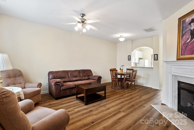 living room featuring arched walkways, wood finished floors, a high end fireplace, visible vents, and baseboards