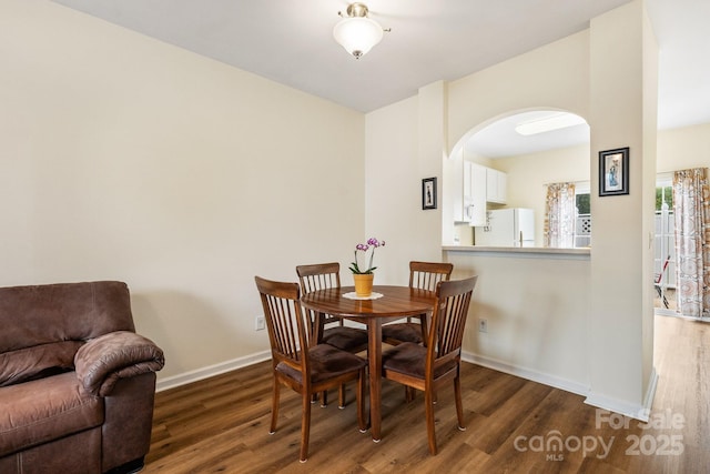 dining space featuring arched walkways, wood finished floors, and baseboards