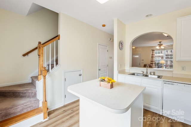 kitchen featuring arched walkways, a sink, light countertops, a center island, and dishwasher