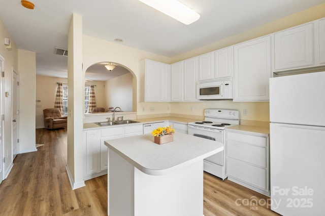 kitchen featuring white appliances, a center island, light countertops, white cabinetry, and a sink