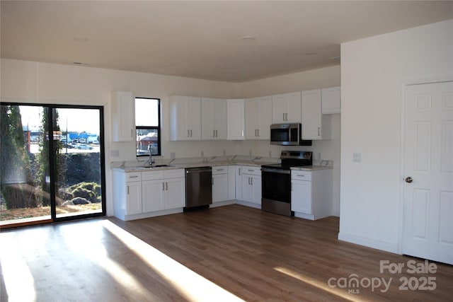 kitchen with stainless steel appliances, wood finished floors, a sink, white cabinetry, and baseboards