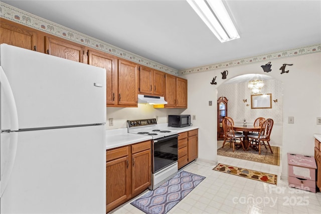 kitchen featuring brown cabinets, under cabinet range hood, white appliances, arched walkways, and light countertops