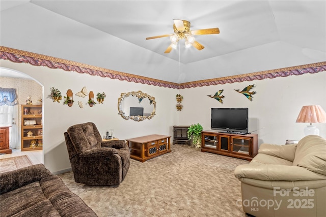 carpeted living area featuring arched walkways, a raised ceiling, a ceiling fan, and vaulted ceiling