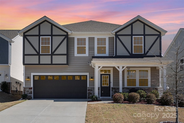 tudor house featuring a shingled roof, a porch, concrete driveway, stone siding, and an attached garage