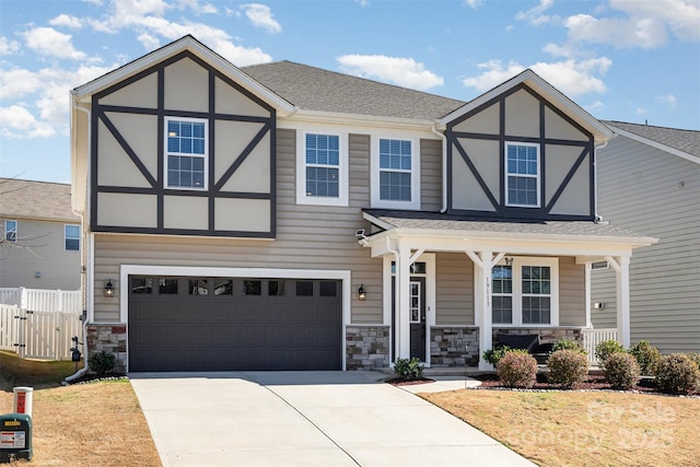 tudor house featuring fence, a porch, a garage, stone siding, and driveway