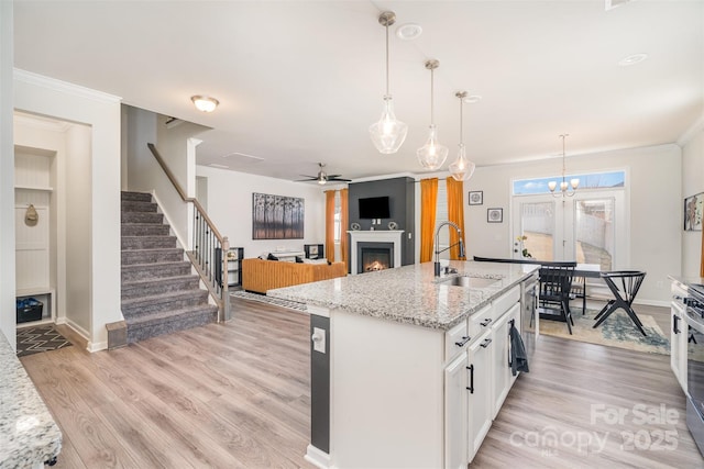 kitchen with white cabinetry, light wood-style flooring, a warm lit fireplace, and a sink