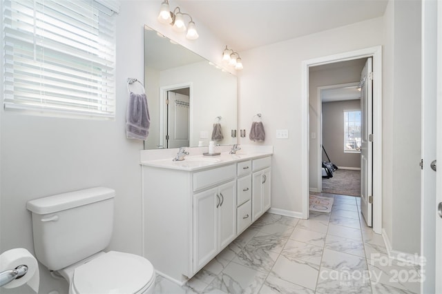 full bath with baseboards, double vanity, a sink, toilet, and marble finish floor