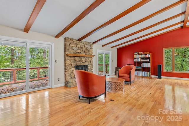 living area featuring lofted ceiling with beams, a stone fireplace, wood-type flooring, and baseboards