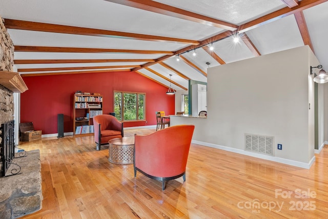 living area featuring baseboards, visible vents, lofted ceiling with beams, a stone fireplace, and light wood-type flooring