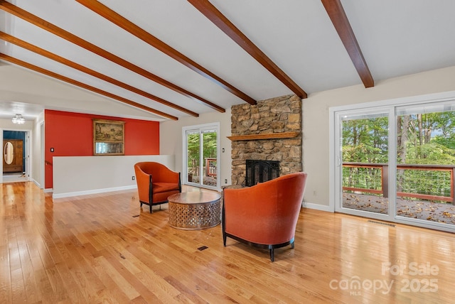 living room with vaulted ceiling with beams, light wood-type flooring, a fireplace, and baseboards