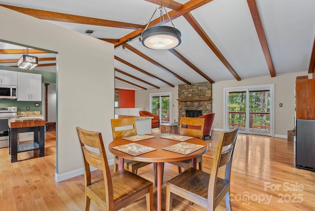 dining space with light wood finished floors, a stone fireplace, baseboards, and vaulted ceiling with beams