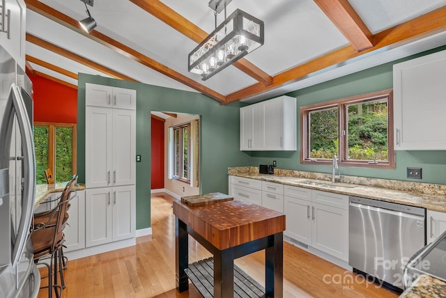 kitchen featuring white cabinets, light stone countertops, stainless steel appliances, light wood-type flooring, and a sink