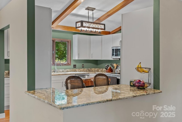 kitchen featuring light stone countertops, beam ceiling, stainless steel microwave, and a sink