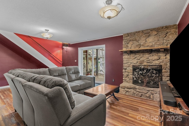 living area with a textured ceiling, a stone fireplace, and wood finished floors