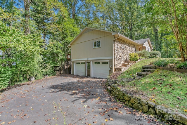 view of home's exterior with an attached garage, stone siding, and aphalt driveway