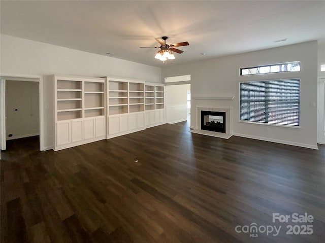 unfurnished living room featuring a ceiling fan, dark wood-style flooring, baseboards, and a tiled fireplace