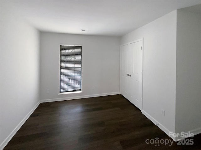 spare room with dark wood-style floors, visible vents, and baseboards