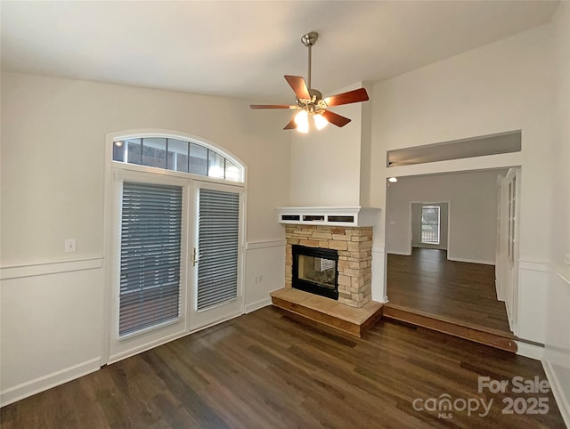 unfurnished living room featuring a towering ceiling, a ceiling fan, wood finished floors, and a stone fireplace