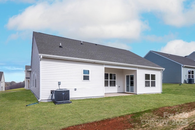 rear view of house featuring cooling unit, roof with shingles, a patio, and a lawn