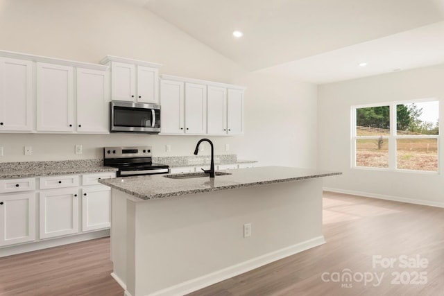 kitchen with stainless steel appliances, a sink, white cabinets, light stone countertops, and an island with sink