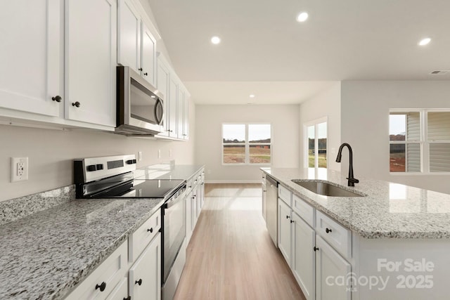 kitchen with recessed lighting, stainless steel appliances, a sink, white cabinetry, and a center island with sink