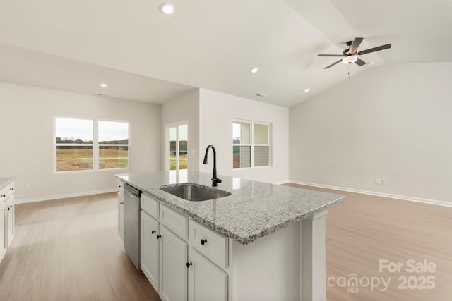 kitchen with a sink, vaulted ceiling, stainless steel dishwasher, light wood finished floors, and a center island with sink