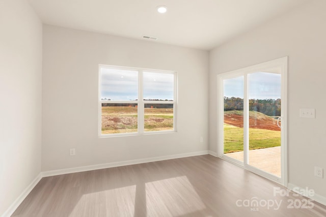 unfurnished room with plenty of natural light, visible vents, baseboards, and wood finished floors