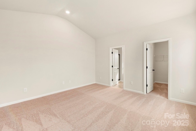 unfurnished bedroom featuring vaulted ceiling, light carpet, a walk in closet, and baseboards