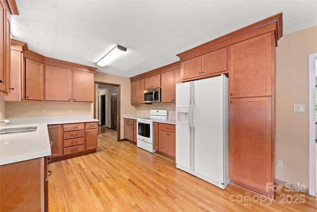 kitchen featuring white appliances, a sink, light wood-style flooring, and brown cabinets