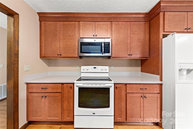 kitchen featuring brown cabinets, white appliances, light countertops, and a textured ceiling