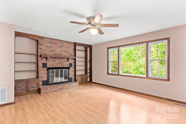 unfurnished living room featuring baseboards, visible vents, wood finished floors, a textured ceiling, and a fireplace