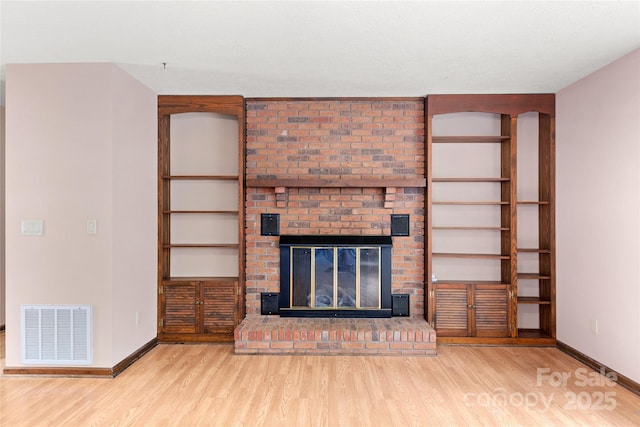 unfurnished living room featuring a brick fireplace, baseboards, visible vents, and wood finished floors