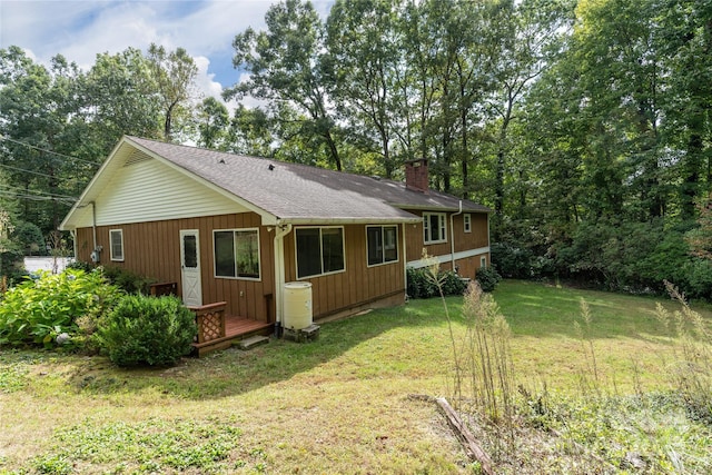 back of house featuring roof with shingles, a chimney, and a yard