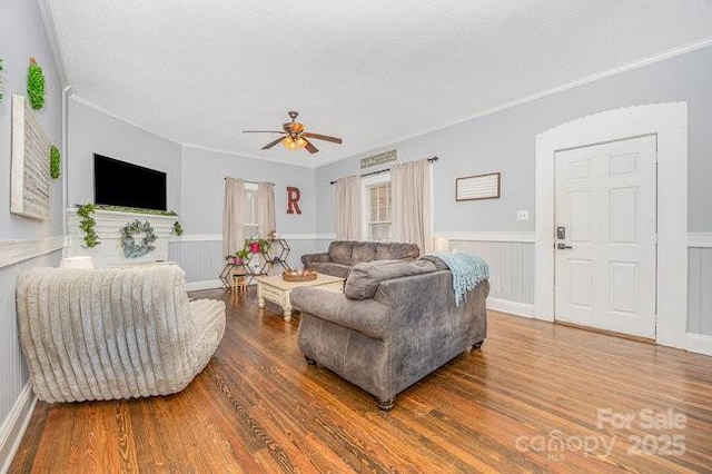 living area with wainscoting, ornamental molding, ceiling fan, and wood finished floors