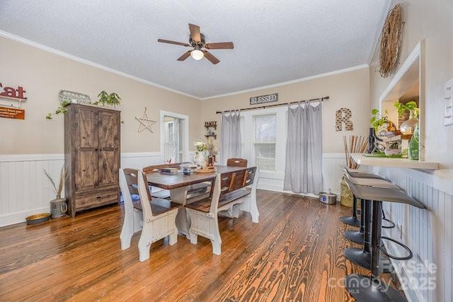 dining room with a textured ceiling, wood finished floors, a wainscoted wall, and ornamental molding