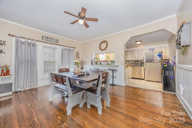 dining room featuring a textured ceiling, light wood-style flooring, ceiling fan, and ornamental molding