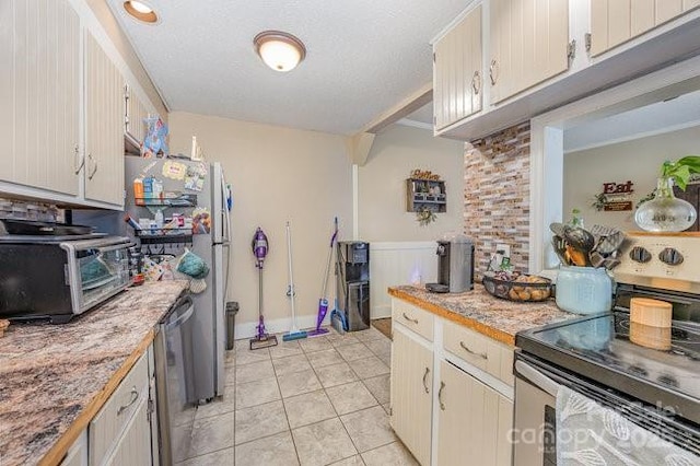 kitchen with light tile patterned floors, a toaster, light countertops, appliances with stainless steel finishes, and a textured ceiling