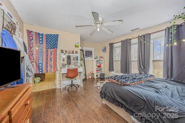 bedroom featuring a ceiling fan, wood finished floors, visible vents, and a textured ceiling