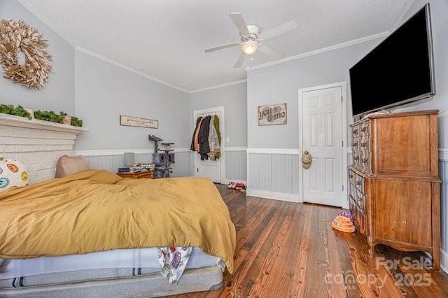 bedroom with crown molding, ceiling fan, wainscoting, wood finished floors, and a closet