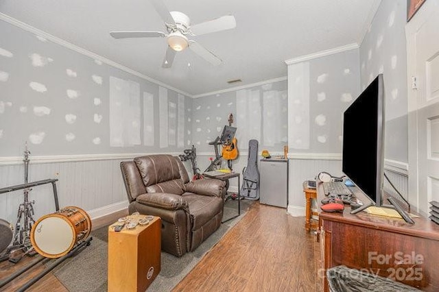 sitting room featuring a wainscoted wall, crown molding, a ceiling fan, and wood finished floors