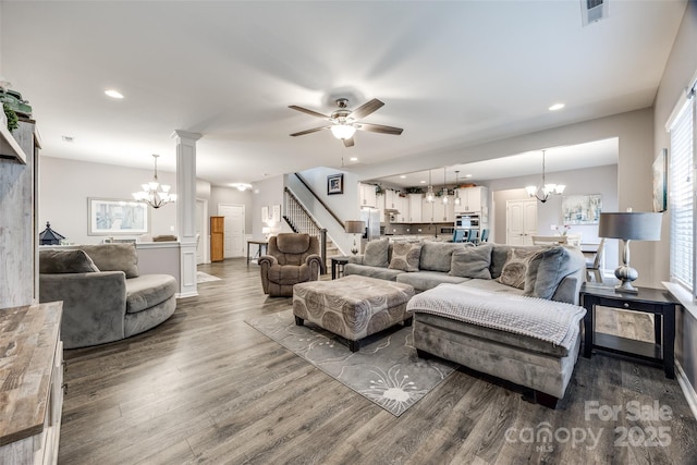 living room with visible vents, wood finished floors, stairs, ornate columns, and ceiling fan with notable chandelier