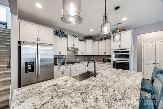 kitchen with appliances with stainless steel finishes, white cabinets, a sink, and tasteful backsplash