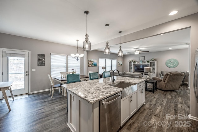 kitchen with dark wood finished floors, appliances with stainless steel finishes, open floor plan, a sink, and light stone countertops