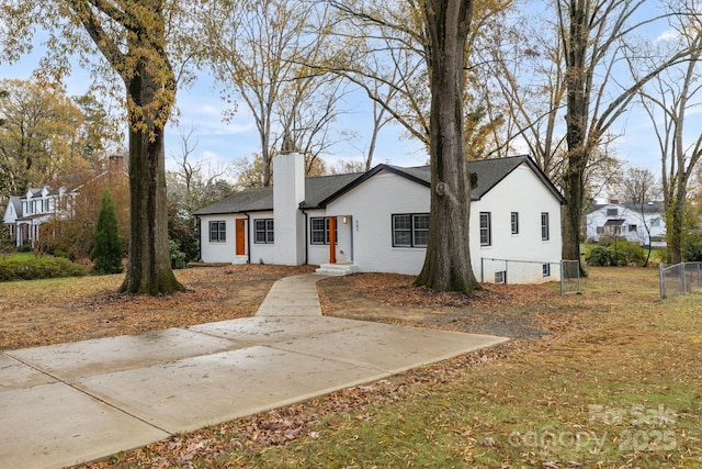 view of front of home with brick siding, a chimney, and fence