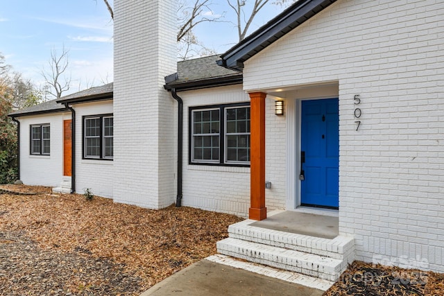 entrance to property featuring roof with shingles, brick siding, and a chimney