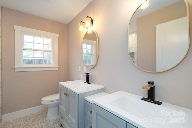 bathroom featuring a sink, two vanities, toilet, and baseboards