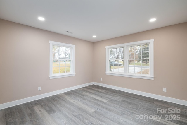 empty room with dark wood-style floors, visible vents, baseboards, and recessed lighting