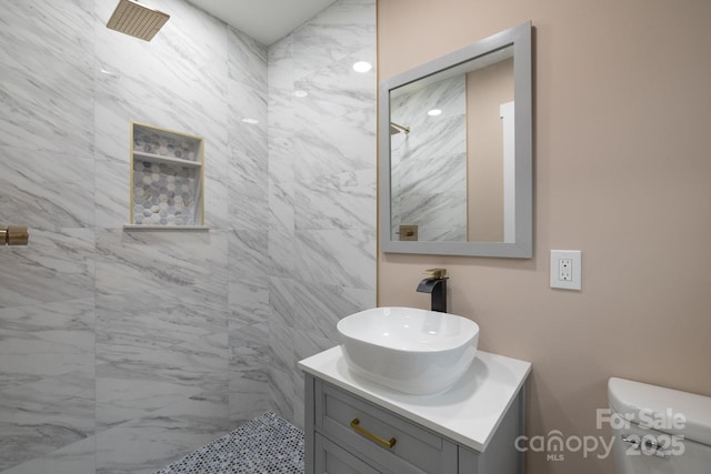 bathroom featuring toilet, a tile shower, and vanity