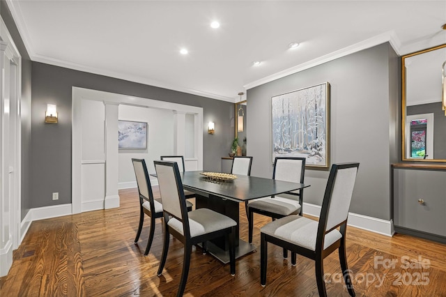 dining area featuring baseboards, wood finished floors, decorative columns, and crown molding